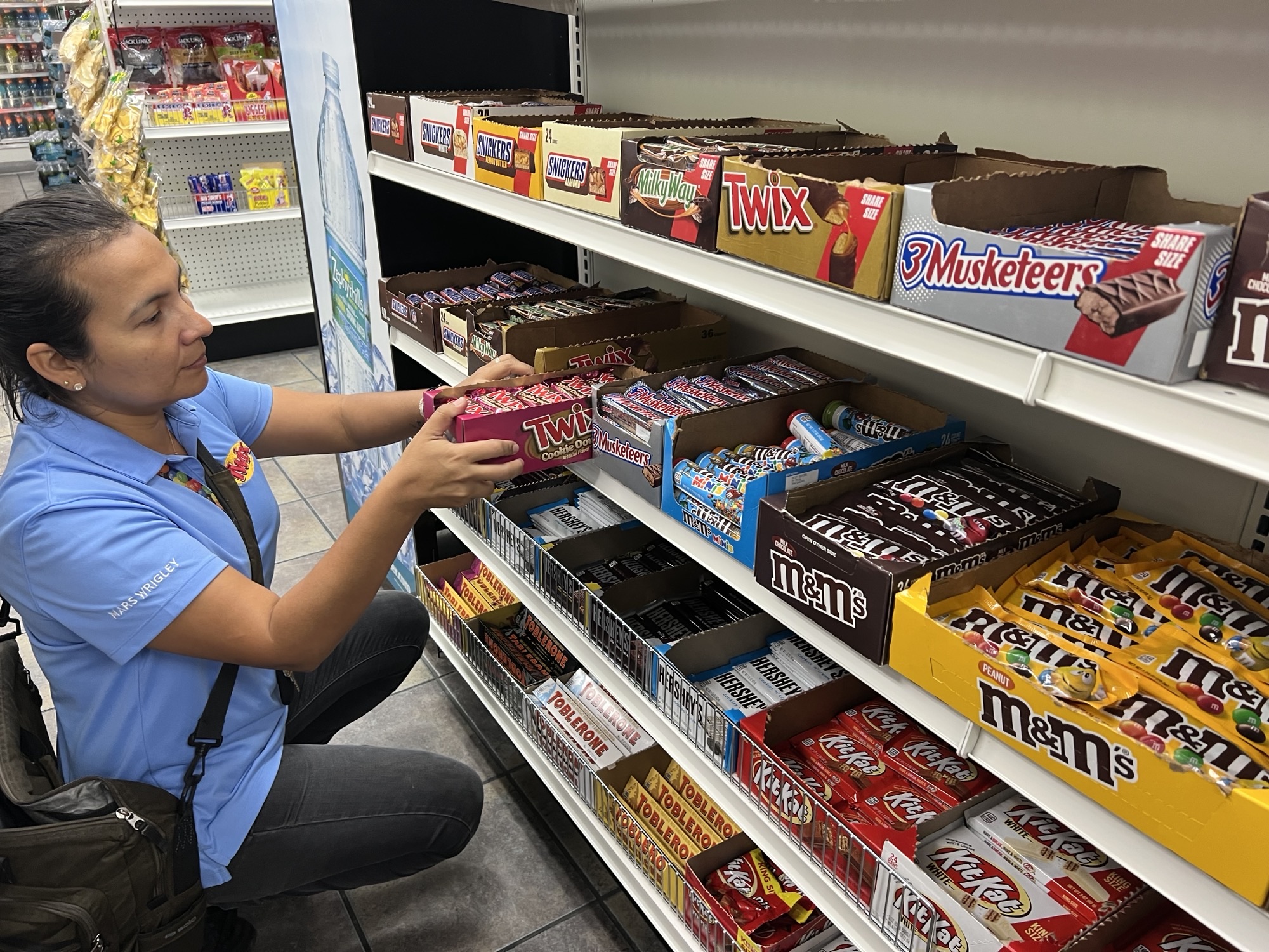 Female merchandising representative stocks product on convenience store shelf